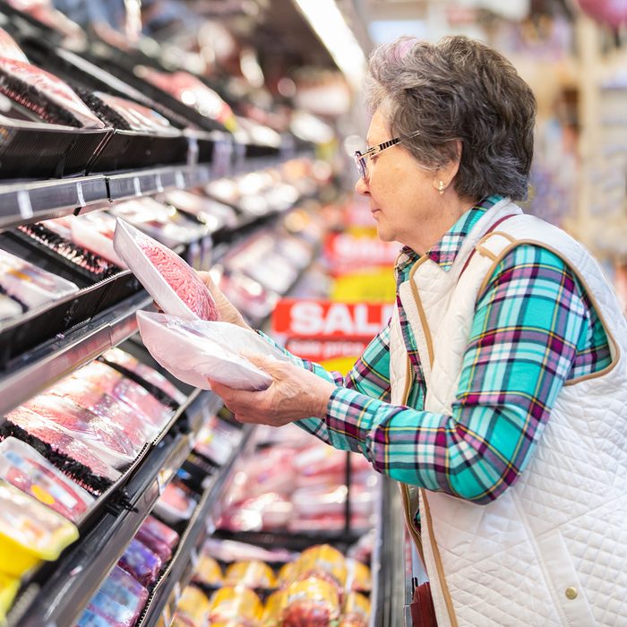 Senior woman comparing prices for meat selection.