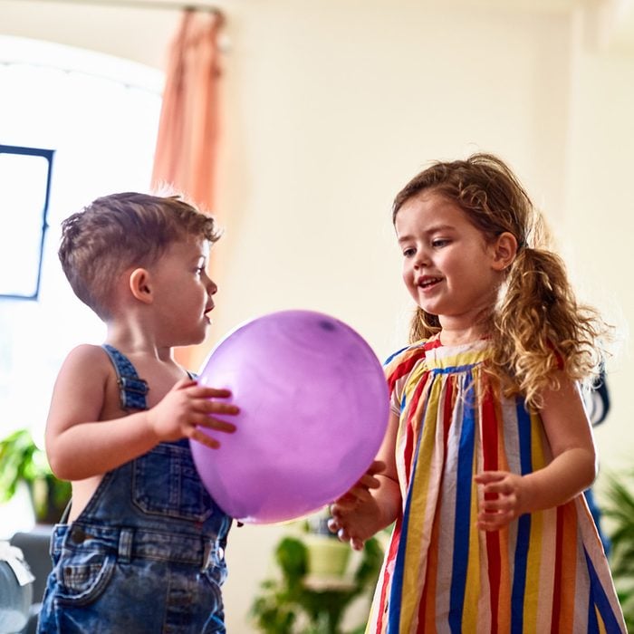 Young boy and girl having fun playing game with purple balloon at home, low angle, sharing, togetherness, friendship