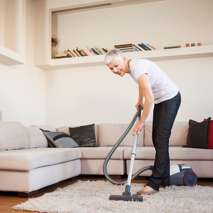 Woman cleaning carpet with a vacuum cleaner in room