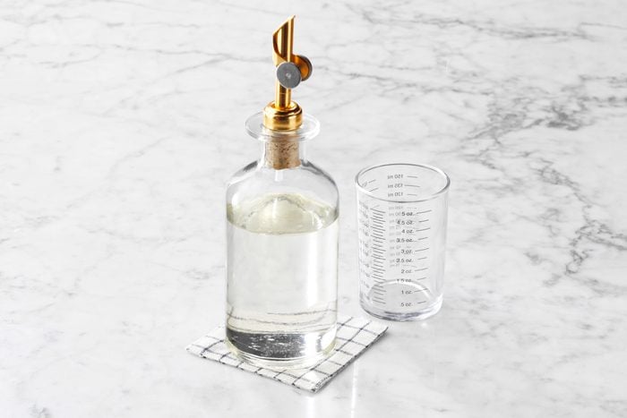 Simple Syrup in a glass bottle with a measuring cup to the side on a white marble kitchen counter top