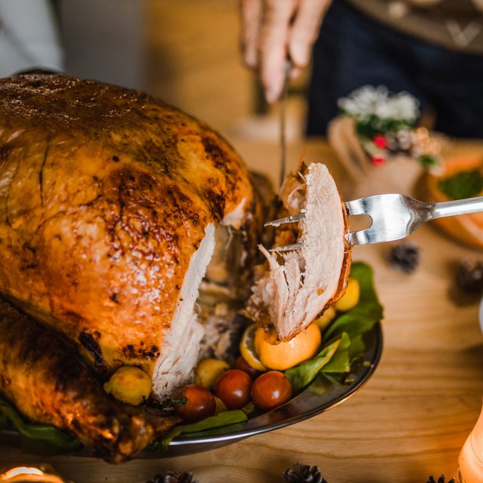 Close up of unrecognizable person carving white meat during dinner at dining table.