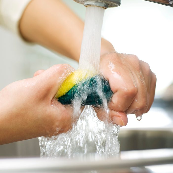 Person rinsing sponge under kitchen faucet