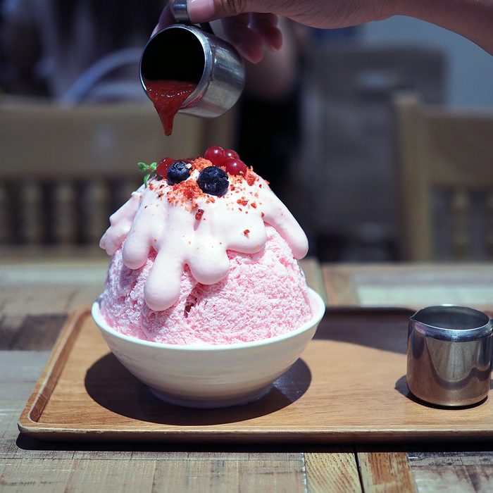 Pour strawberry sauce over a pink milk kakigori or Japanese shaved ice dessert flavored, Topped with pink whipped cream, blueberry and red currant, same as Bingsu Korean dessert.