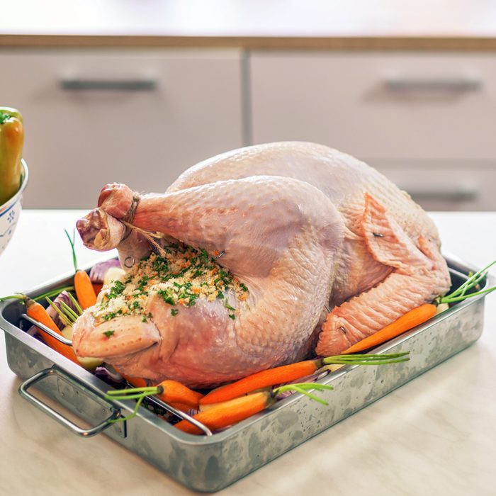 Raw turkey surrounded with side dishes in baking sheet ready to be prepared for Holidays