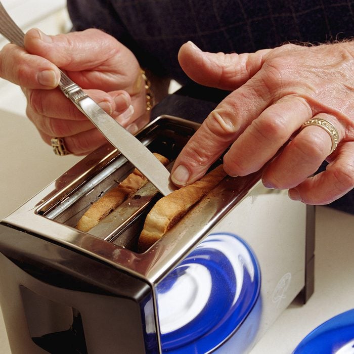 Senior man getting toast out of toaster with knife, close-up
