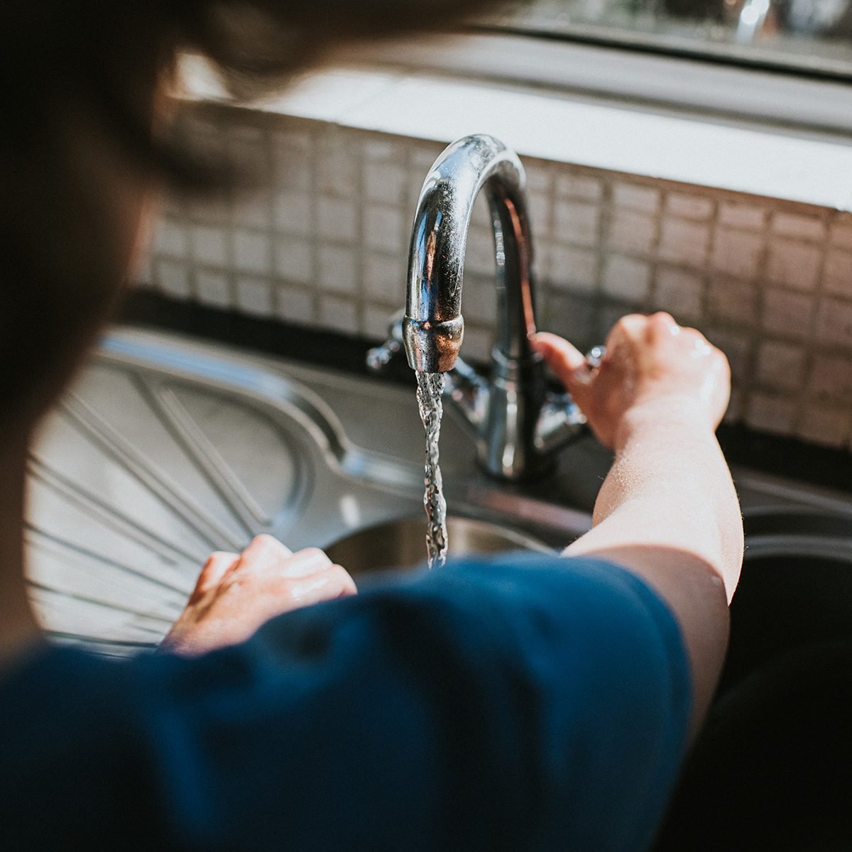 Someone turning the tap on to wash their hands at a kitchen sink.