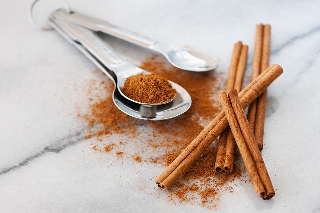 cinnamon sticks and ground cinnamon in silver measuring spoons on a marble countertop surface