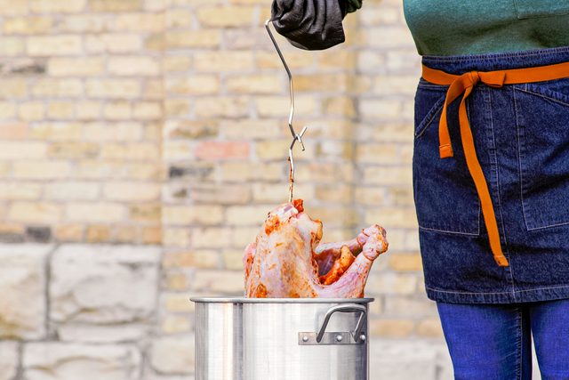 Someone Holding a Marinated Turkey in Metal Pot to Deep Fry it