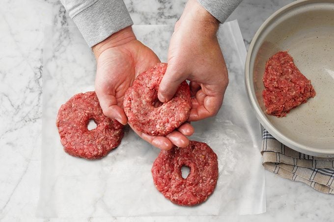 Easy Grilled Hamburgers; How to; marble surface; overhead camera angle; marble surface; burgers; burger; hamburger; hamburgers; hands; prep; in process; mixing bowl; ground beef; patty; patties; wax paper; step #3 hand forming hole in center of burger patty; raw beef; uncooked
