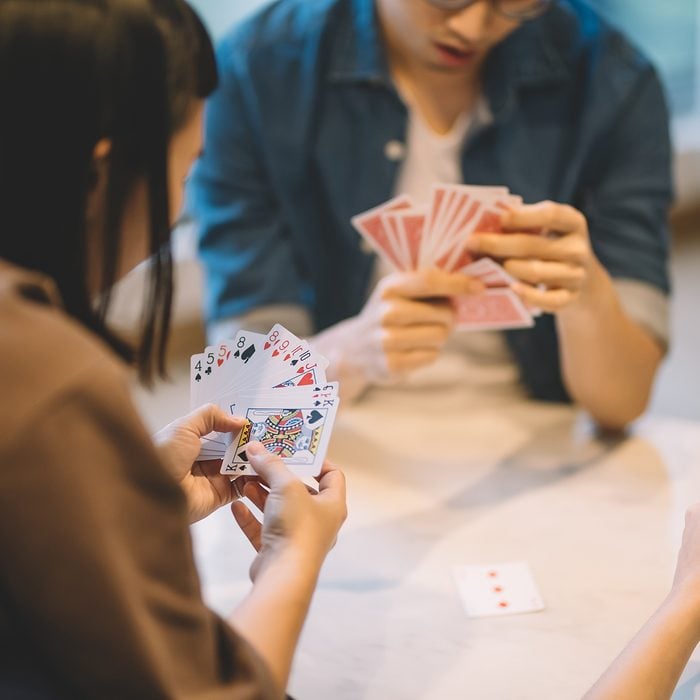 asian chinese friends playing poker cards game in living room