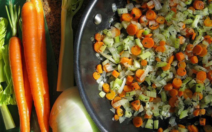 chopped Mirepoix in a cooking pan with carrots, celery and onion on the side on a kitchen counter