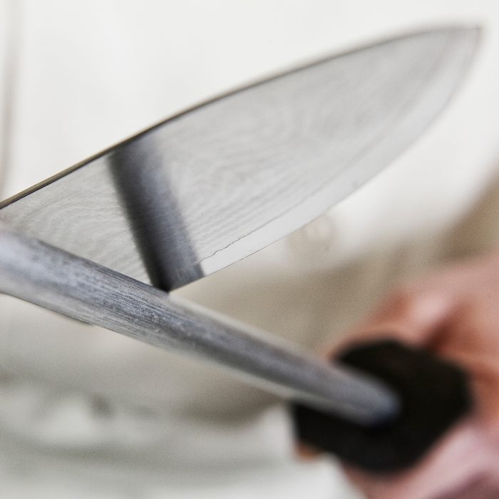 Close-up of a chef sharpening a large kitchen knife blade with a steel.