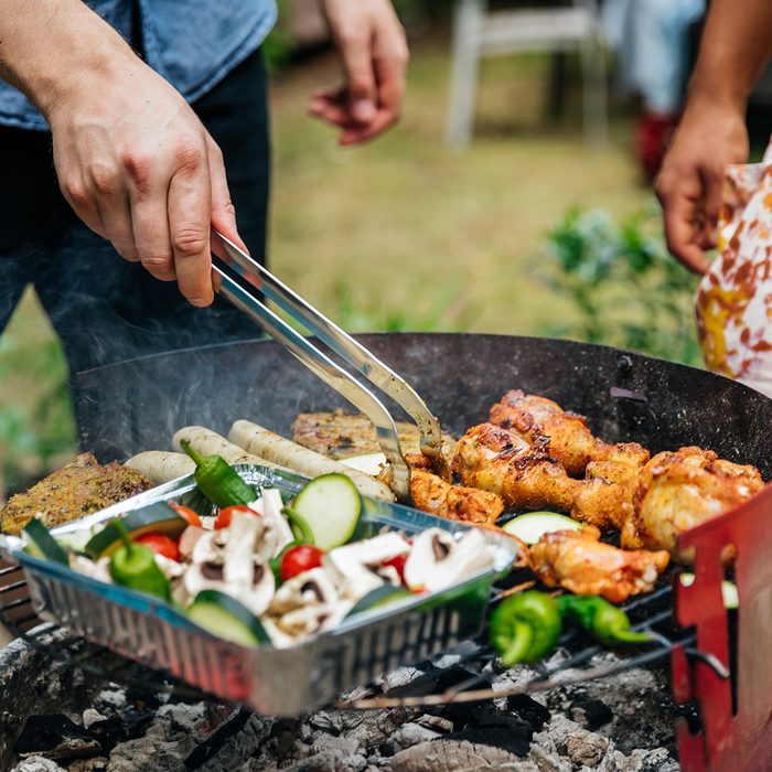 A close up of aman cooking different foods on a barbecue.