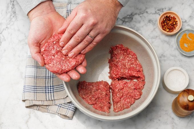 Easy Grilled Hamburgers; How to; marble surface; overhead camera angle; marble surface; burgers; burger; hamburger; hamburgers; hands; prep; in process; mixing bowl; ground beef; patty; patties; wax paper; step #2 disk of meat divided with four sections marked; one section removed and being formed into patty with hands; raw beef; uncooked; spices; spice; salt; red pepper flakes; striped cloth; cloth
