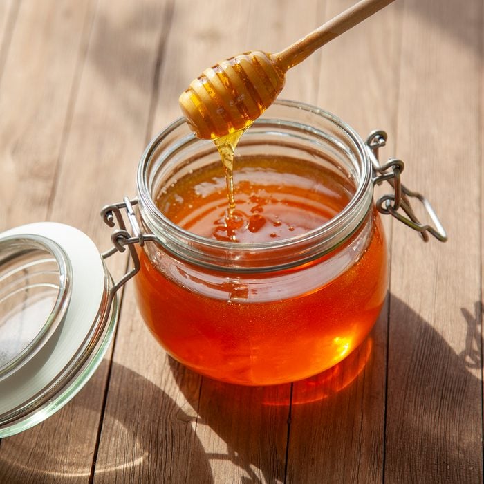 Pot Of Honey And Wooden Stick Are On A Table outdoors.