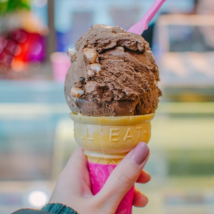 Hand holding a scoop of chocolate marshmallow ice cream in a cone.