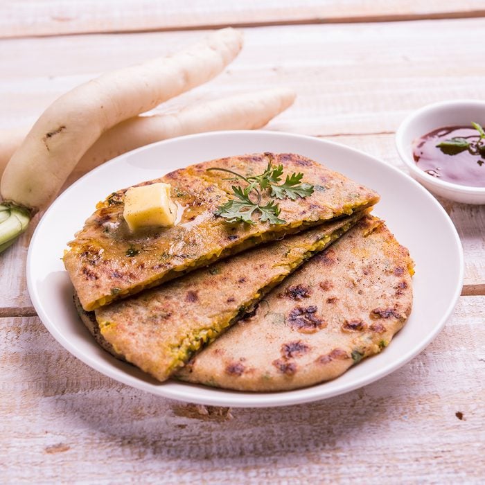 Daikon, radish, mooli or muli paratha or stuffed radish paratha, indian or pakistani favourite recipe served with butter and tomato ketchup, selective focus