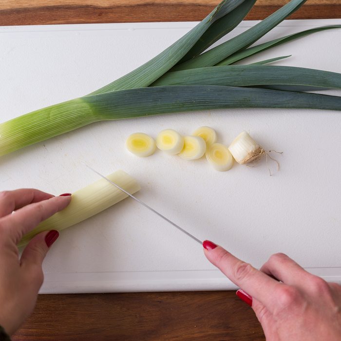 Hands of person slicing leeks on white cutting board, healthy eating concept