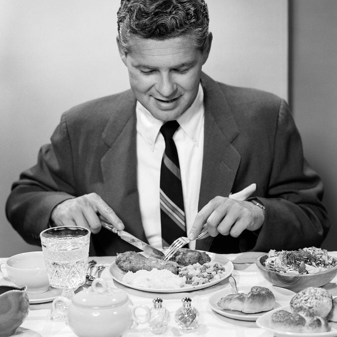 1950s SMILING MAN IN SUIT AND TIE SITTING AT TABLE HOLDING KNIFE AND FORK EATING DINNER (Photo by H. Armstrong Roberts/ClassicStock/Getty Images)