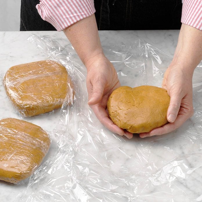 A person's hands wrapping cookie dough in plastic wrap.