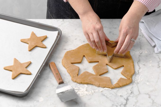 Hands using a star-shaped cookie cutter to cut cookie dough.