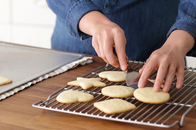 Hands transferring cutout cookies to a wire cooling rack.