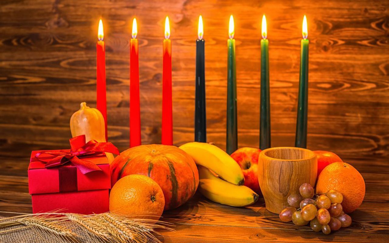 Kwanzaa holiday concept with traditional lit candles, gift box, pumpkins, ears of wheat, grapes, orange, banana, bowl and fruits on wood background