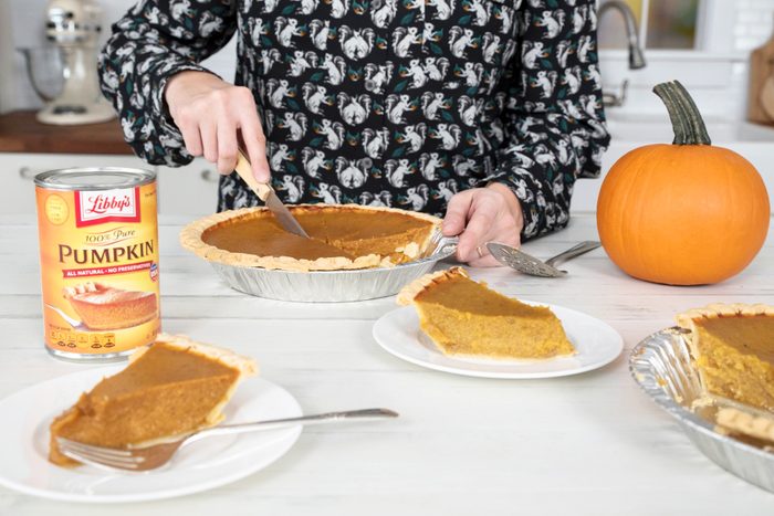 close up of a woman cutting a a pumpkin pie with plates of slices in the foreground