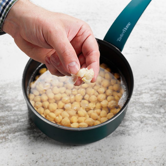 A person removing the skins from a pot of chickpeas in order to make homemade hummus.
