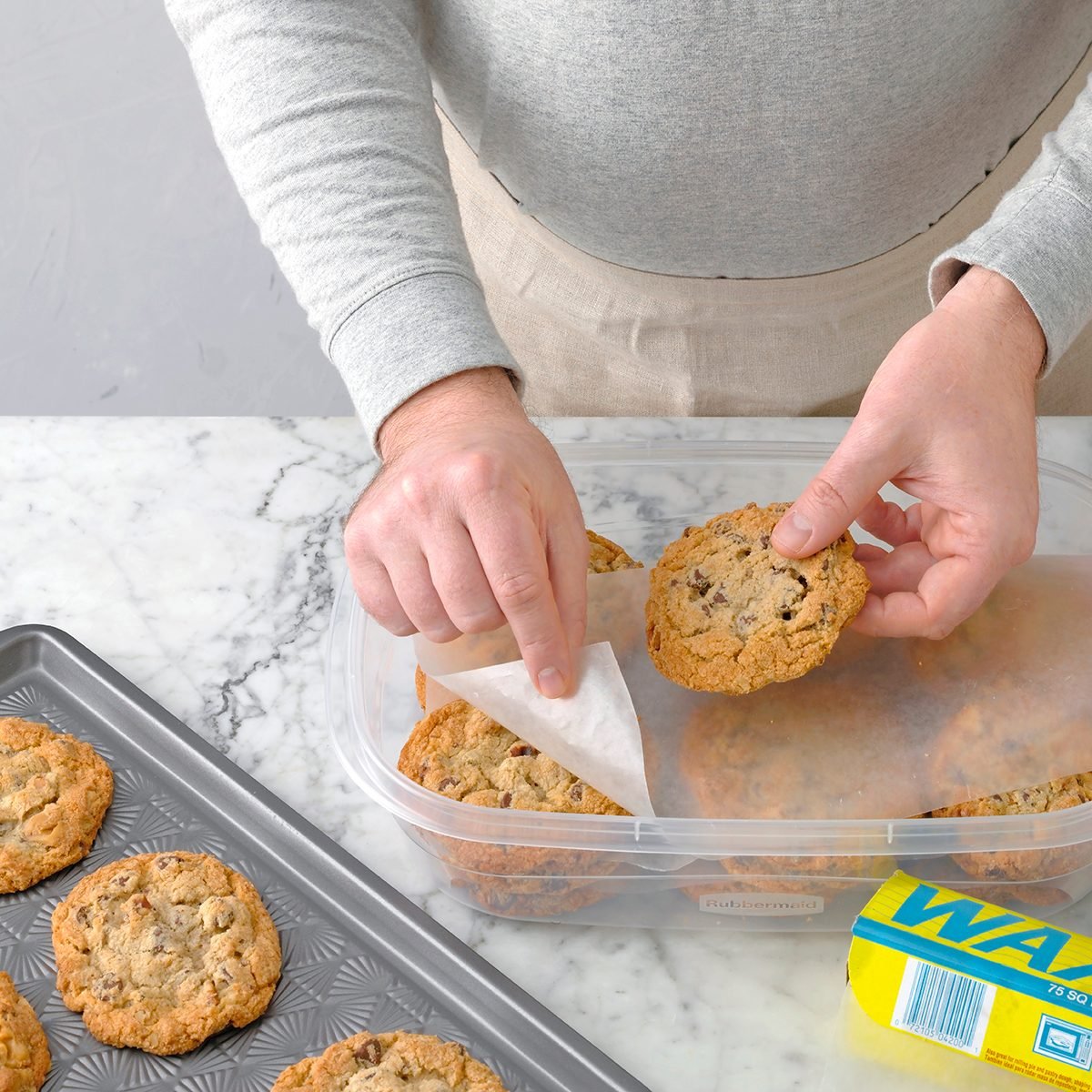 A person layering homemade cookies on parchment paper to store them in an airtight container.