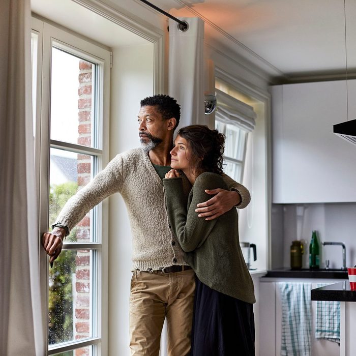 Pensive man embracing young woman looking out of window in kitchen