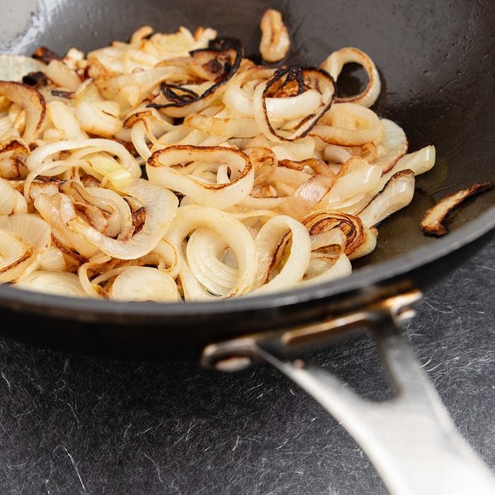 Sautéing and caramelising sliced onions in black wok. Black decorative surface. High point of view.