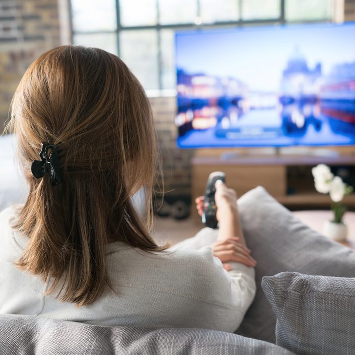 Woman relaxing at home watching tv and holding the remote control