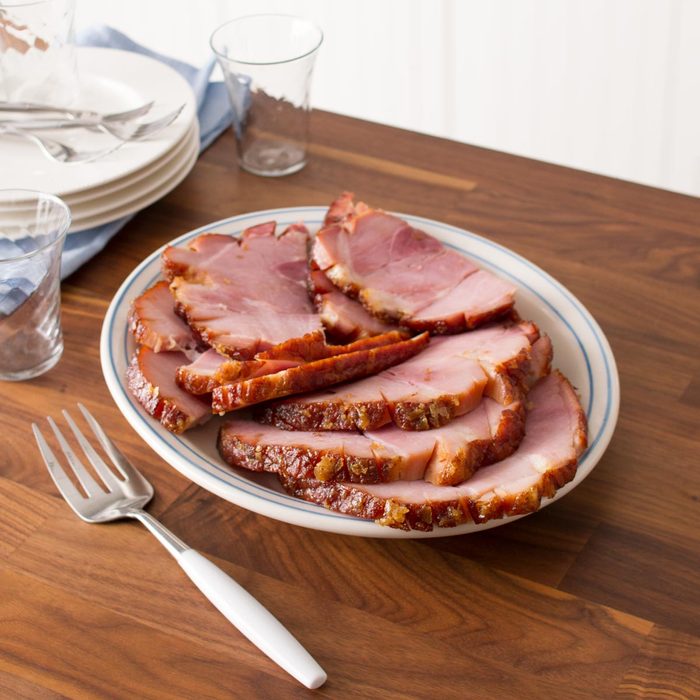 plate of carved ham on a wood countertop near a stack of plates in a kitchen