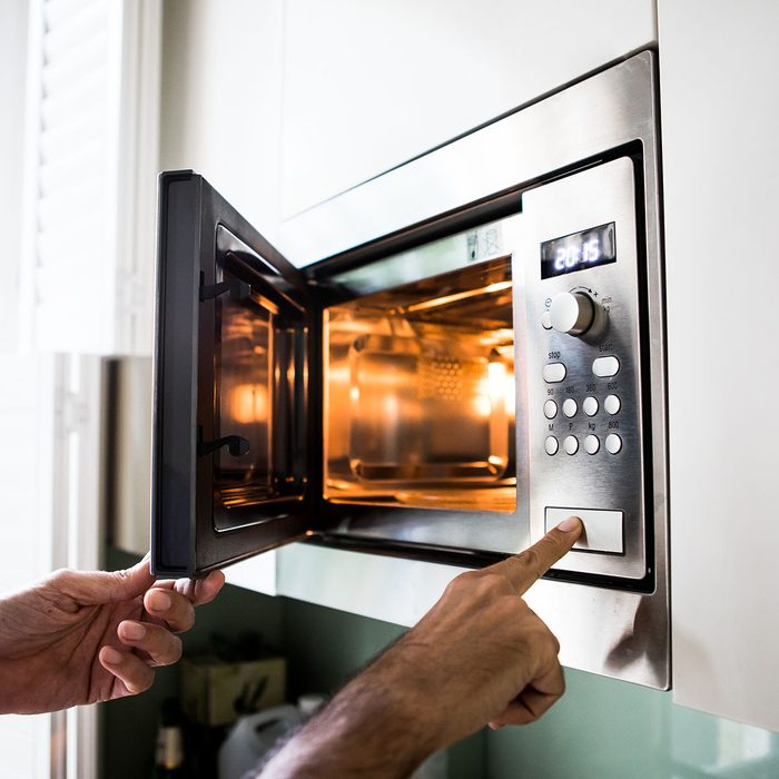 A man using a microwave oven. His finger on the opening button.