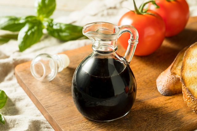 Balsamic Vinegar in a glass container on a cutting board with tomatoes and garlic bread