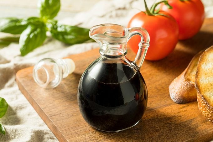 Balsamic Vinegar in a glass container on a cutting board with tomatoes and garlic bread