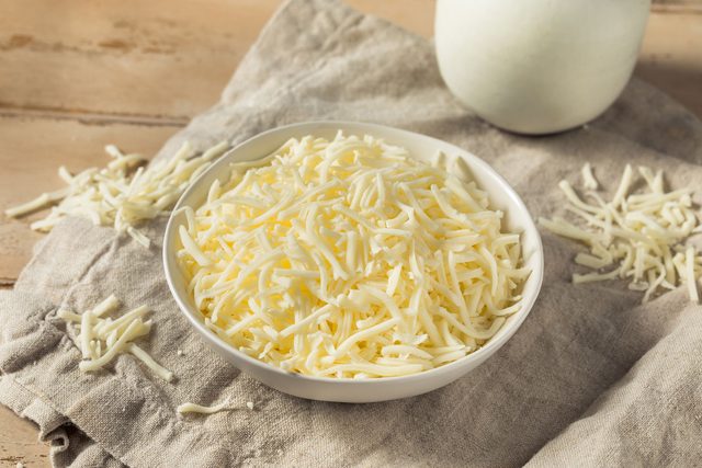 Shredded Mozzarela Cheese in a bowl over a kitchen cloth on a wooden table