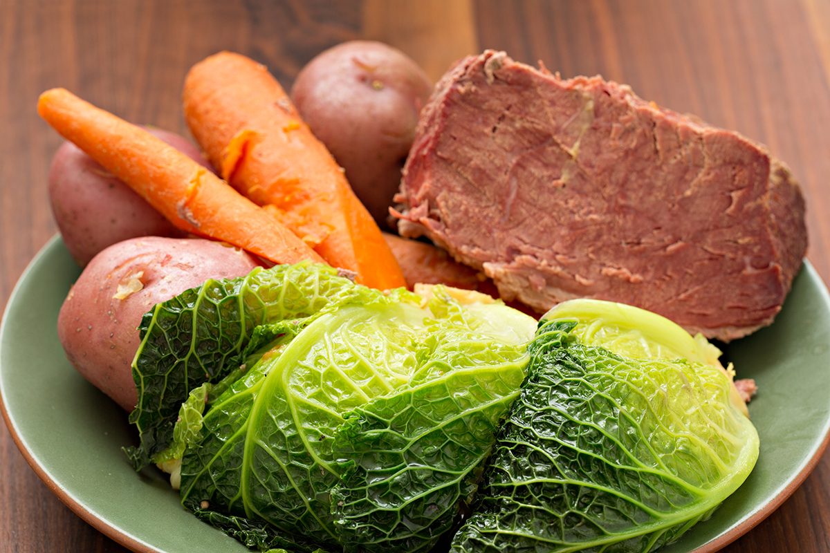 A high-angle close-up of some corned beef, cabbage, carrots and red potatoes on a green plate.