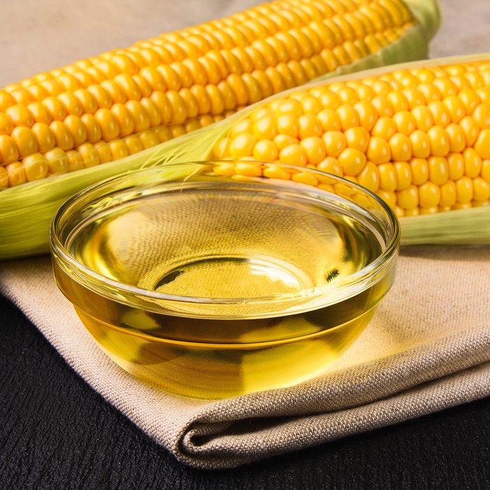 Fresh corn oil in a bowl with ears of corn on a cloth on a slate background