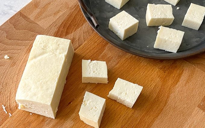Fresh paneer cut into cubes and blocks placed on a cutting board and serving tray