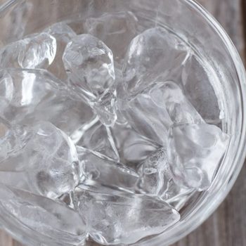 horizontal image of a clear glass bowl with ice cubes on a wooden background