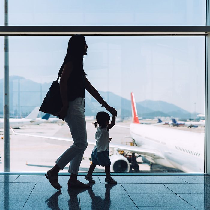 Silhouette of joyful young Asian mother holding hands of cute little daughter looking at airplane through window at the airport while waiting for departure uses for reusable bags