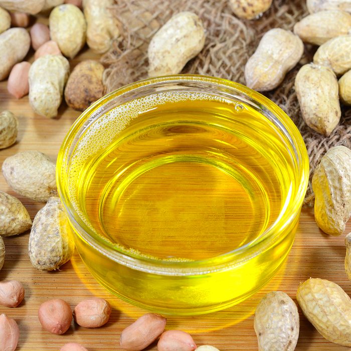 Peanut oil also known as groundnut oil in a glass cup and peanuts on the background.