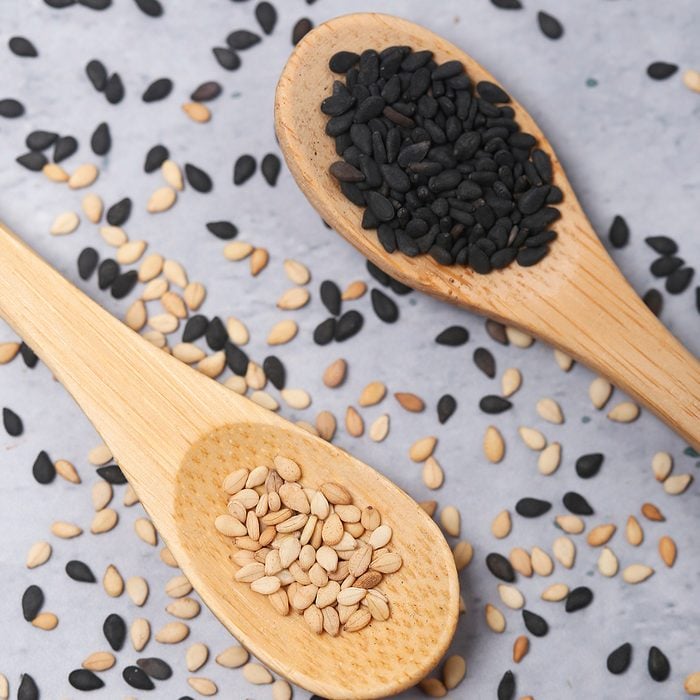 Sesame and black sesame in wooden spoons on cement background