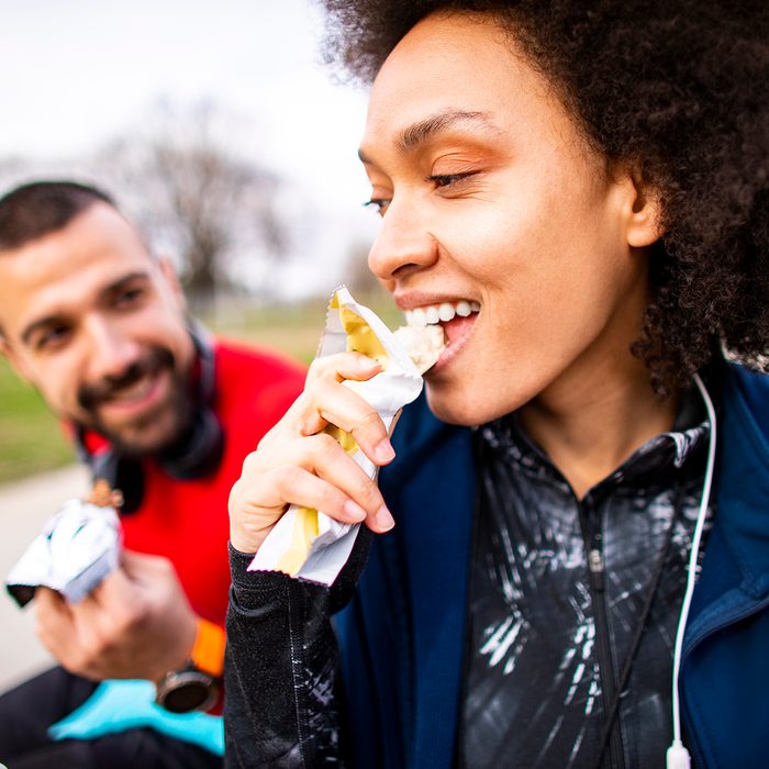 Young athletic woman enjoying a protein snack with her partner while sitting on a park bench keto snack bars