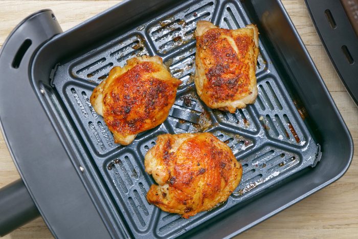 Four chicken breasts in an air fryer on a wooden table