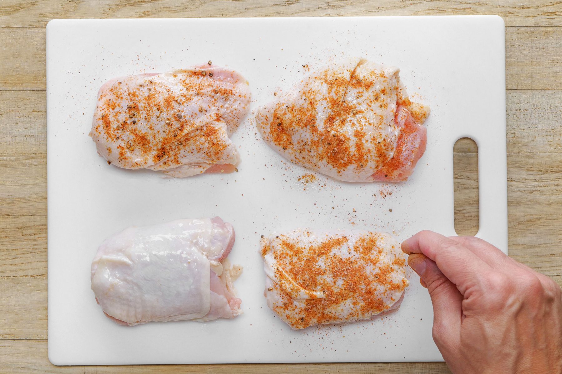 Four chicken breasts with seasoning on a cutting board