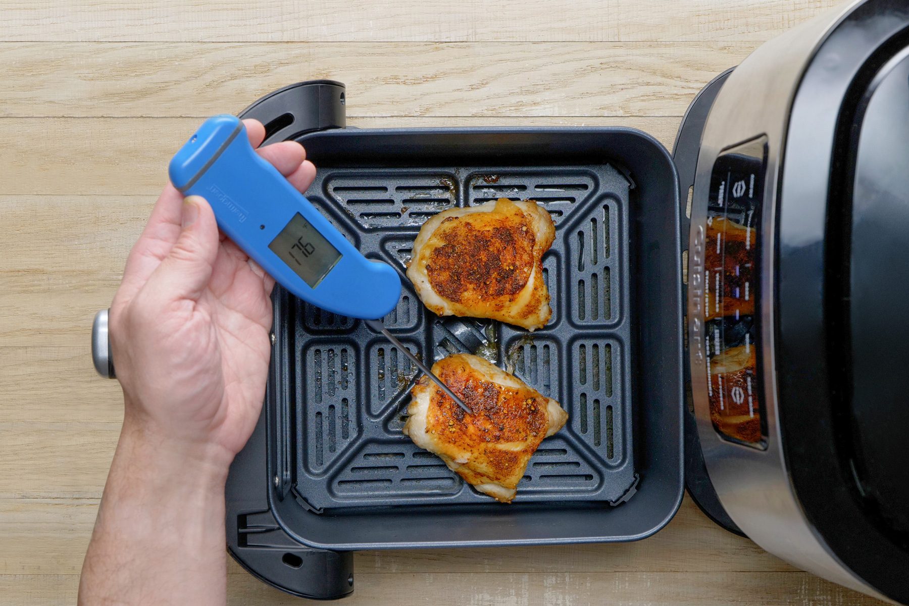 A person using a thermometer to check the temperature of chicken in an air fryer