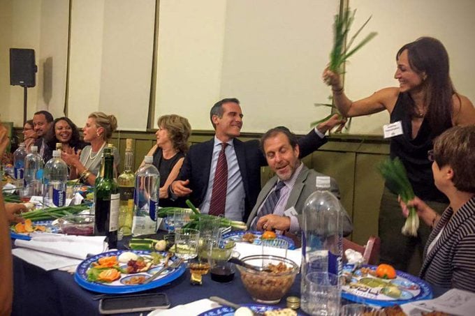 A group of people playfully whipping each other with scallions during a Passover seder. This Passover tradition is unique to Jews from Afghanistan and Iraq.